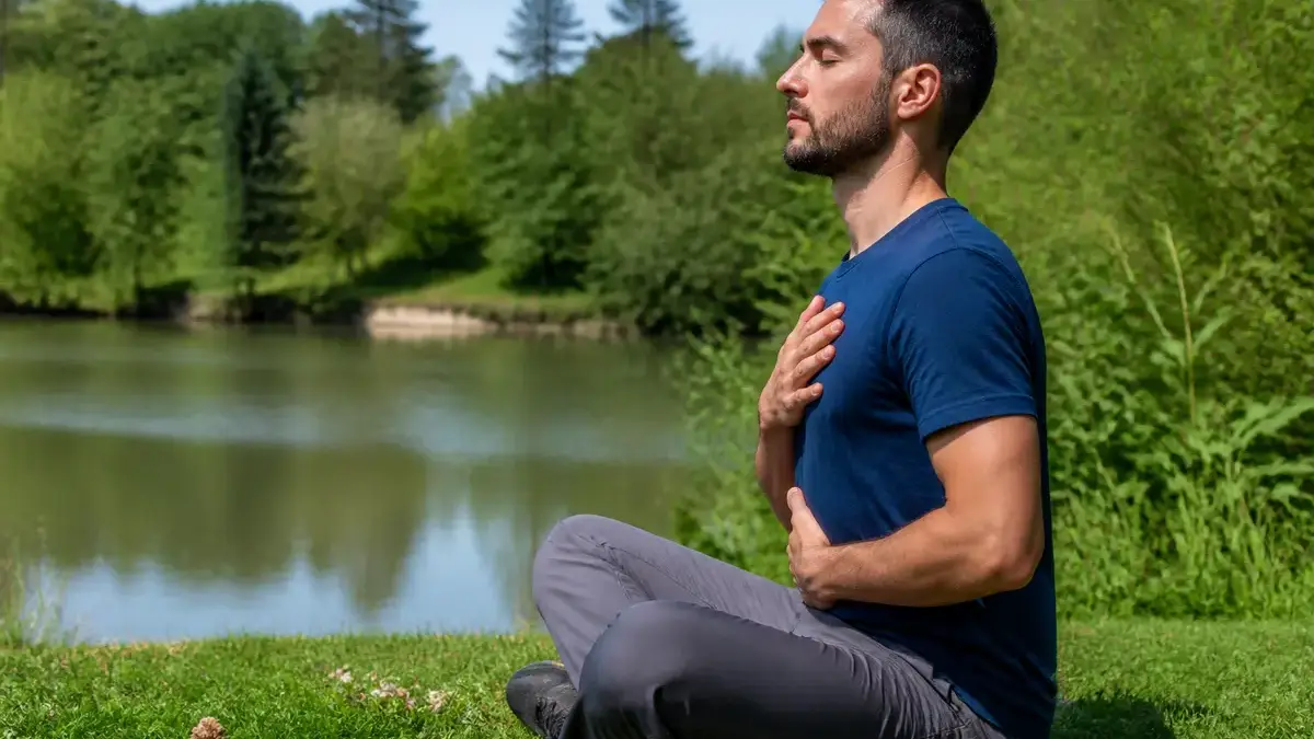 Homme méditant au bord d'un lac, pratiquant l'exercice de cohérence cardiaque.
