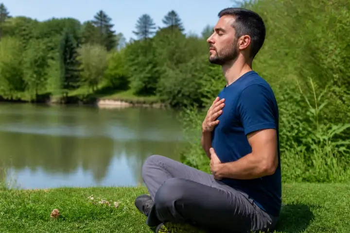Homme méditant au bord d'un lac, pratiquant l'exercice de cohérence cardiaque.