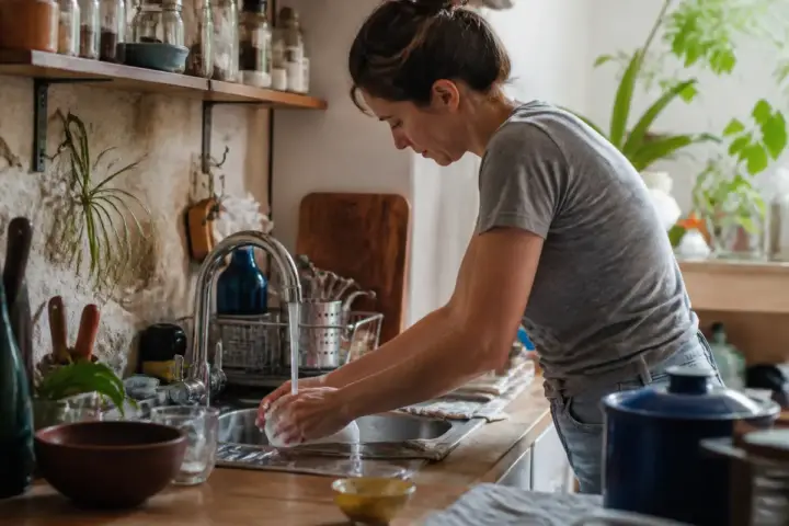 Femme lavant une assiette dans une cuisine avec les 4 accords toltèques en esprit